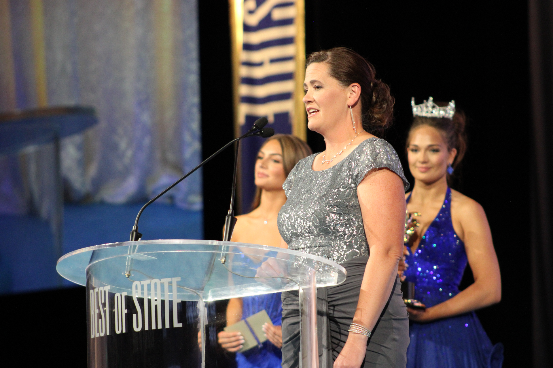 A gala honoree speaks from the podium as Miss Utah royalty stands just behind.