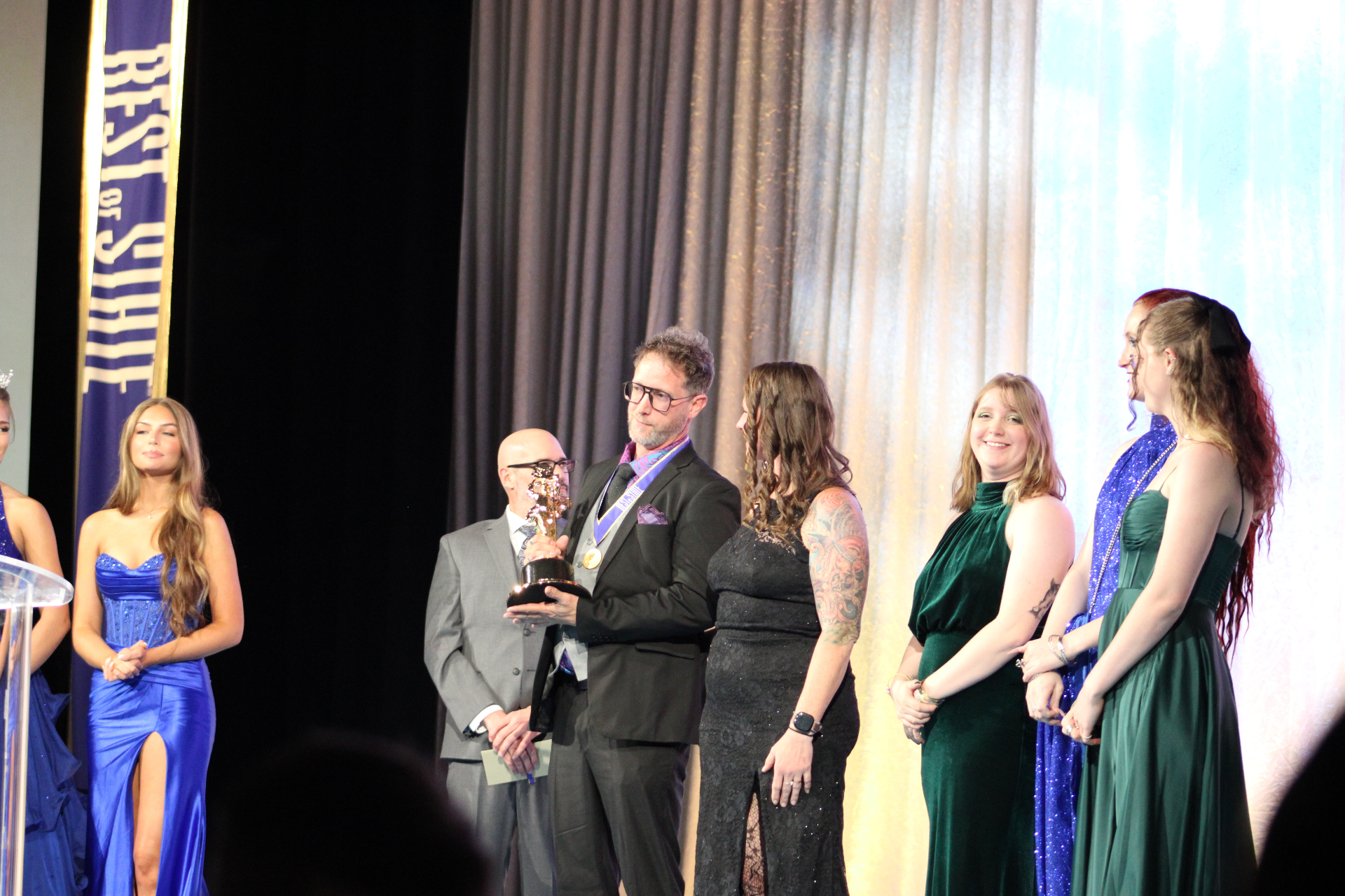 A 2026 medalist holds the BOSS® statue surrounded by presenters and Miss Utah royalty.