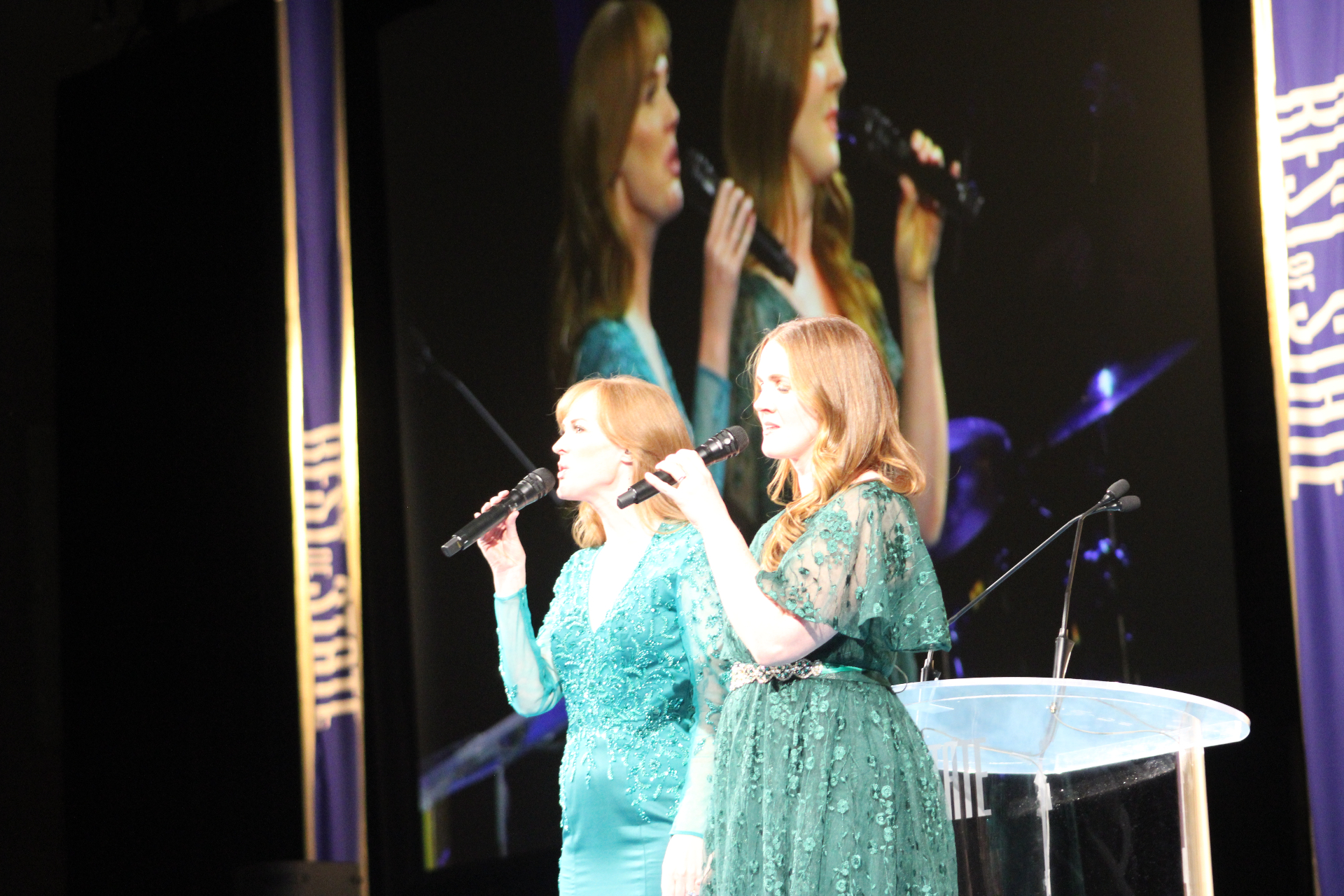 Live vocal performance fills the room as the gala stage glows behind the singers.